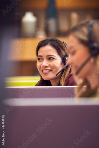Mature Businesswoman Wearing Phone Headset Talking To Caller In Busy Customer Services Centre