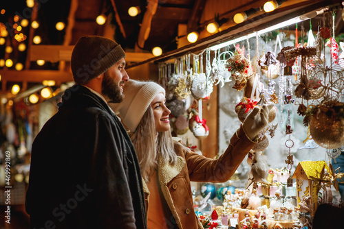 Christmas, winter holidays, vacation, travel, purchase conception: happy smiling couple shopping at festive street market, choosing gifts. Outdoor night portrait. Copy, empty space for text 