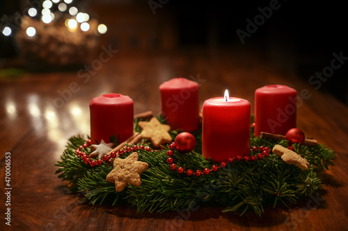 First Advent - decorated Advent wreath from fir branches with red burning candles on a wooden table in the time before Christmas, festive bokeh in the warm dark background, copy space, selected focus