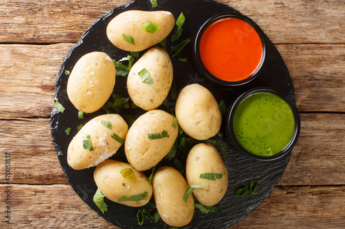 Canarian Wrinkly Potatoes Papas Arrugadas with a mojo rojo and mojo verde sauces close up in the plate on the table. Horizontal top view from above
