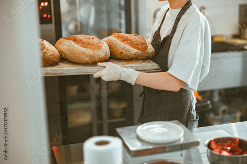 Woman holds tray with large breads standing in spacious craft bakery