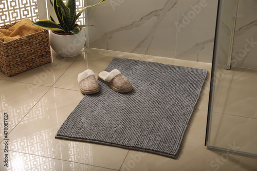 Soft grey bath mat and slippers on floor in bathroom