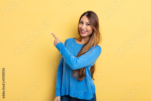 asian pretty woman looking excited and surprised pointing to the side and upwards to copy space