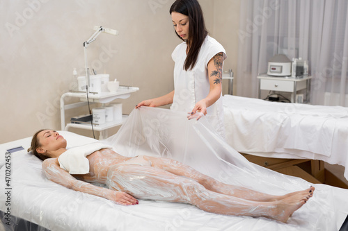 Cosmetic procedure wraps. The beautician covers the young girl with cellophane for anti-cellulite hydro-massage in a modern cosmetology room. Moisturizing body mask and body wrap.