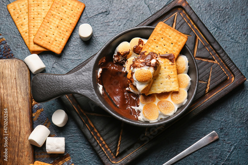 Frying pan with delicious S'mores dip and crackers on dark background