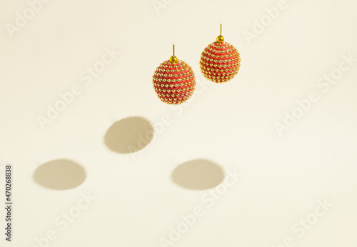 Two shiny red and gold baubles hovering above the beige background with shadows. 70s and 80s retro concept. Minimalist Christmas and New Year composition. Copy space.