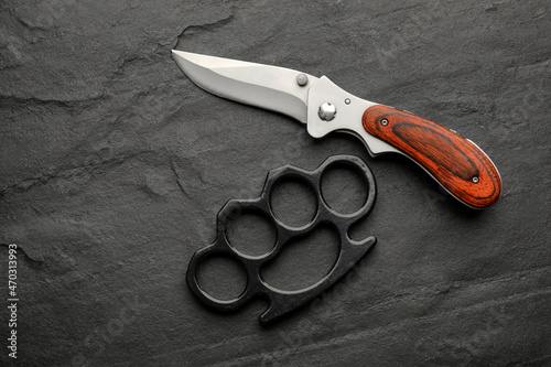 Brass knuckles and knife on black background, flat lay