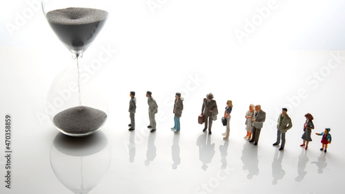miniature people. different people are walking next to the hourglass on a white background. lifespan of humanity