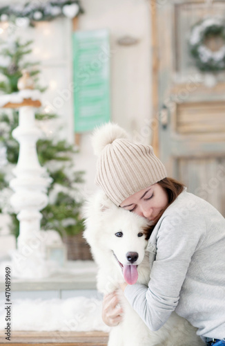 girl hugging a white fluffy samoed dog near front door of a house decorated for christmas