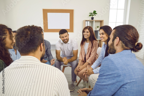 Different people sitting in a circle, talking and smiling during a group therapy session. Team of happy cheerful positive young and mature men and women having a meeting