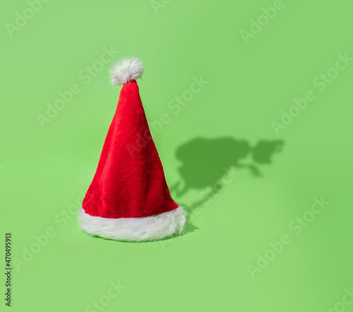 Grinch shadow stealing Christmas behind Santa's cap on bright green background.