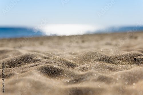 Sandy coast close-up against the background of sun glare of the sea. Narrow selective focus on sand and blurred background.