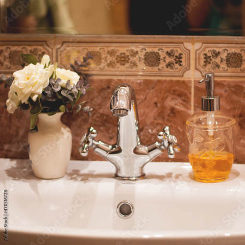 silver shiny faucet in the bathroom on a background of brown tiles, flowers and soap