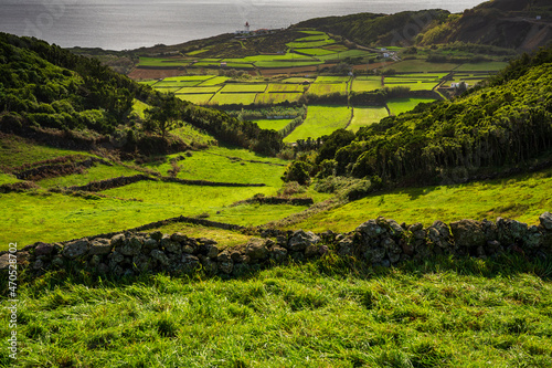 Typowy zielony krajobraz wyspy Teiceira, Portugalski archipelag Azory. W tle widać latarnie morską Ponta das Contendas i koźlą wyspę.