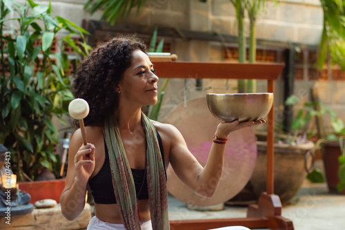 Hippy latina woman doing a performance with a tibetan bowl and stick at home