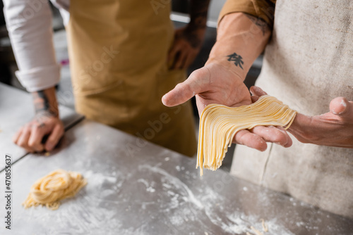 Cropped view of chef holding raw spaghetti near colleague in kitchen