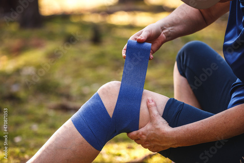 First aid after hiking accident. Injured hiker putting elastic bandage to her knee. Tendon problems or sprain knee during trekking in nature