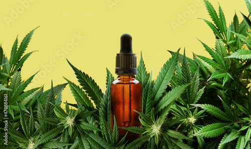 Glass dropper bottle of cannabis oil with marijuana plants and yellow background