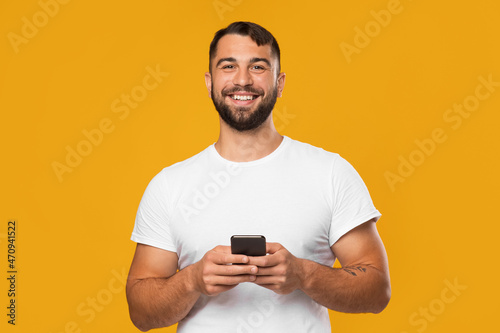 Satisfied mature european man in white t-shirt typing on smartphone and chatting in social network