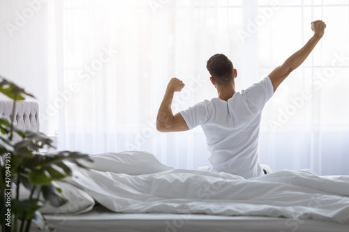 Man Stretching In Bed After Waking Up In The Morning, Rear View