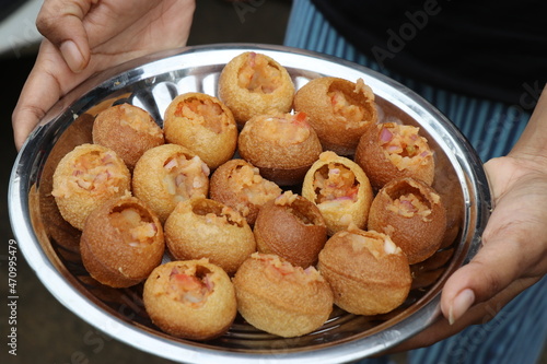 Hand holding a plate of homemade gol gappa or a few call as Pani puri balls stuffed with potato and ready to be eaten with mint water and sauce