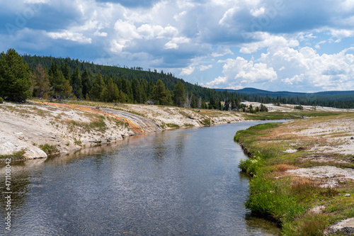 Green grass, trees, and rock line the Firehole River in Yellowstone National Park in Wyoming on a sunny summer day