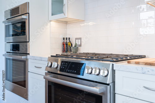 Modern kitchen details of stainless steel gas stove, double oven and white tile backsplash.
