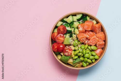 Salmon, avocado, cucumber, tomato, edamame beans and rice poke bowl on pink blue background