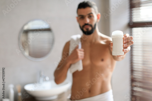 Handsome young guy standing with deodorant bottle in hand