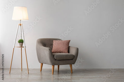 Comfortable armchair with pink pillow, glowing lamp on floor on gray wall background in office or living room
