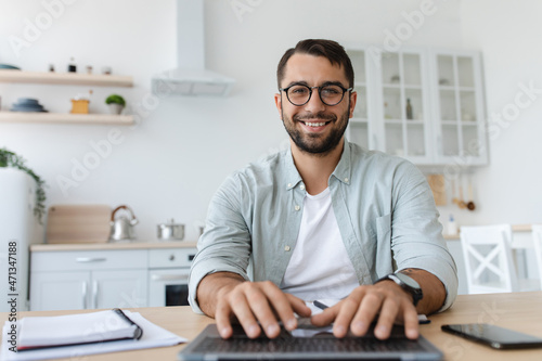 Cheerful mature caucasian male with beard in glasses typing on keyboard, work on laptop, look at webcam
