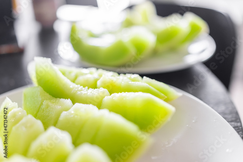 Closeup of vibrant colorful yellow green honey honeydew melon cut slices on white plates for sharing eating macro bokeh
