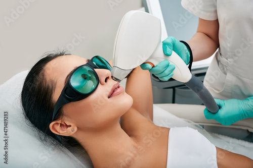 Attractive woman wearing protective glasses while laser hair removal and laser epilation to lips area on her face at a beauty salon