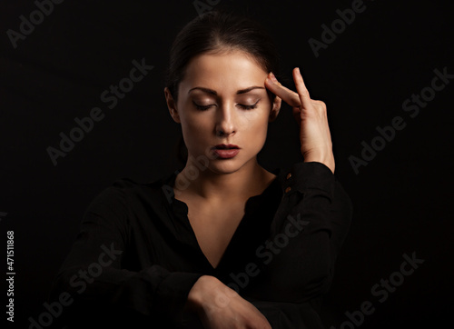 Business strong thinking woman find the answer in clever mind with closed eyes with fingers near the face in black t-shirt on dark shadow black background. Closeup