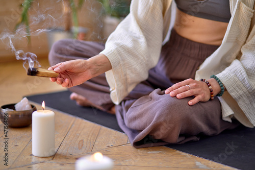 close-up woman Burning palo santo for home purification and meditation, sitting on mat on floor, alone. in domestic cozy atmosphere at day time. yoga practitioner Relax after Yoga training