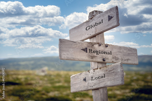 global regional local text quote on wooden signpost outdoors in nature. Blue sky above.