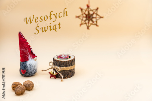 Pocztówka świąteczna z napisem Wesołych Świąt i beżowym tłem, orzechami, drewnianą świeczką i zabawnym skrzatem