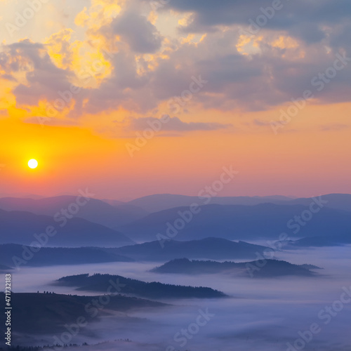 mountain ridge silhouette in blue mist at the sunrise, early morning mountain valley scene