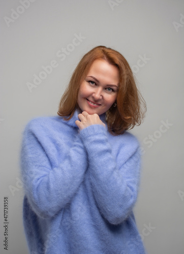 the girl with golden hair wrapped herself in a sweater. gray background.
