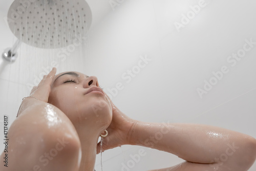 Mujer joven de pelo negro en la ducha con el agua cayendo sobre su cara en primer plano.