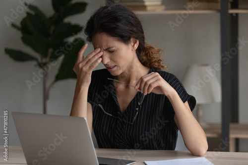 Sudden eye pain. Tired overworked latin woman office employee wince rub nose take spectacles off feel headache eye strain dizziness. Fatigue young female overloaded by computer work has vision problem