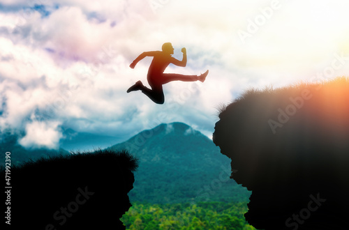 The silhouette of a man jumping over a chasm between rocks. In the background, the ocean and the sky. The concept of freedom, success and overcoming obstacles