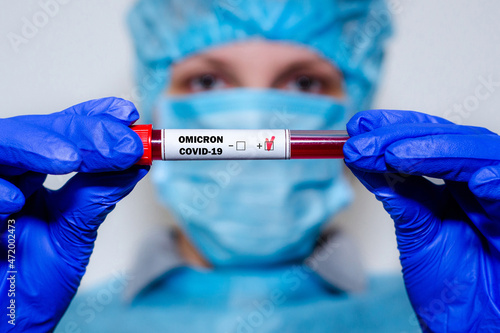 Medical laboratory assistant holding test tube with positive Omicron COVID-19 test blood sample.