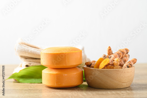 Turmeric soap and fresh turmeric root in a bowl on wooden table with white background, herbal organic soap for skin care