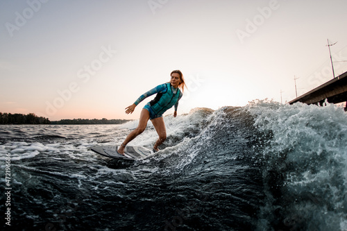 beautiful woman wakesurfer riding down the splashing wave on warm day