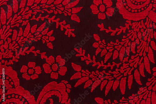 Red lace fabric with floral pattern against black bacground. Texture of embroidery red guipure. Lacy textile for clothes and underwear retro design. Abstract vintage lace pattern. Macro.