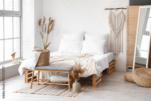 Interior of light bedroom with soft bench and dry reeds in vases