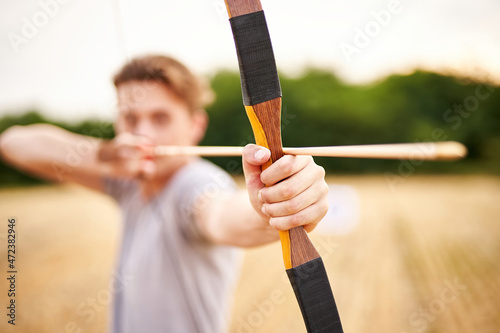 Young male sportsman targeting with traditional bow - Teenager archer practicing archery in nature - Outdoors sports and recreation concept with a millennial boy - Focus on the archer's hand