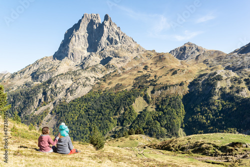 Family day at the mountains in french Pyrenees. Father, mother and baby sitting on a meadow while enjoy views of Pic du Midi d'Ossau. Mountain travel vacation.