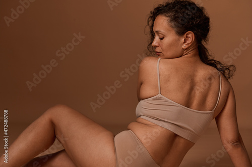 Beautiful overweight woman in lingerie with skin flaws, cellulite and stretch marks after childbirth due to unhealthy lifestyle, posing on a beige background with copy space. Body positive concept